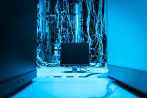 A complex network of cables in a data center with a dark monitor in the foreground.